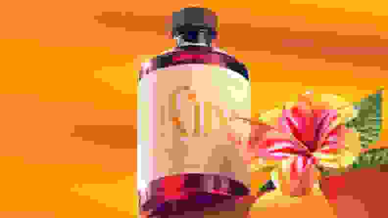 A bottle of alcohol-free elixir by the brand Kin Euphorics against a soft orange backdrop, accompanied by an orange tropical flower.
