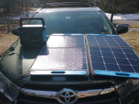 Person using small generator and solar powered panel on top of hood of car.