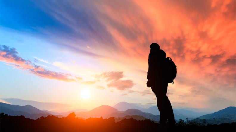 An image of a person staring at a sunset while hiking.