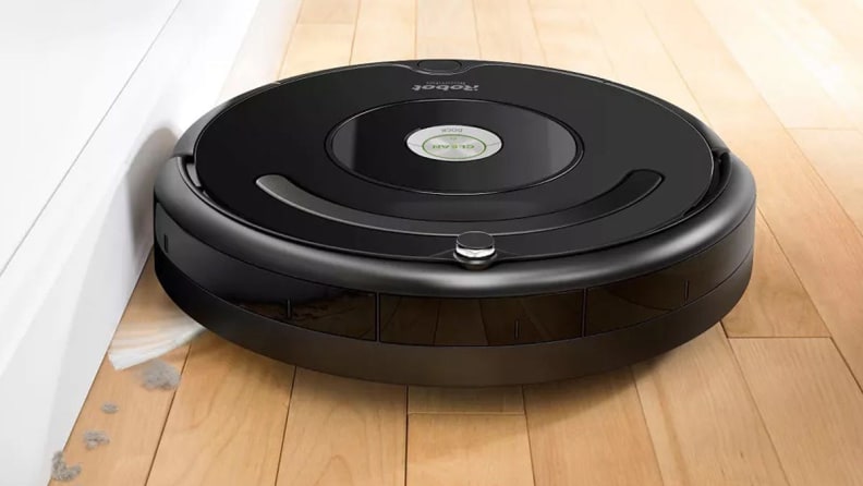 An iRobot Roomba vacuuming the baseboard of a hardwood floor.