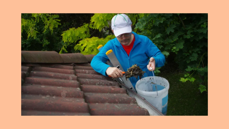 Man on a ladder cleaning gutter on the roof with a trowel and bucket