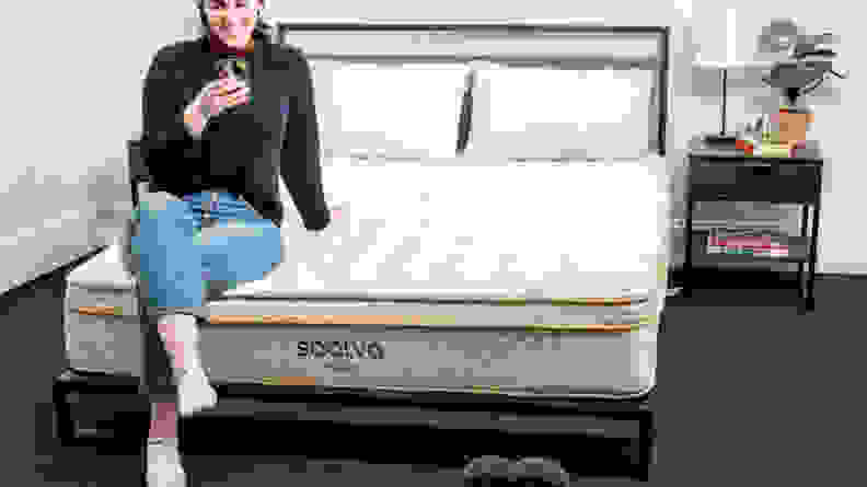 A person sitting on the bottom edge of the Saatva Classic mattress.