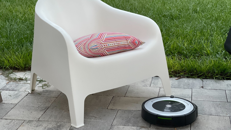 An iRobot vacuum on a patio with a chair in the background.