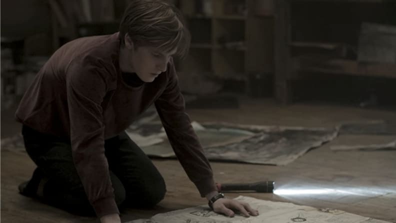 A still from 'Dark' featuring a young man kneeling over a map on the floor.