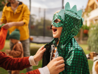 A young  boy dressed in a green dinosaur costume laughing