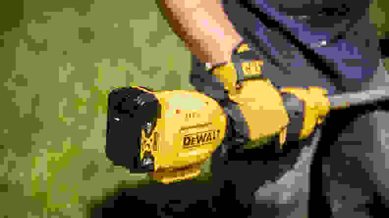 A man holds a weed wacker with a battery pack at one end