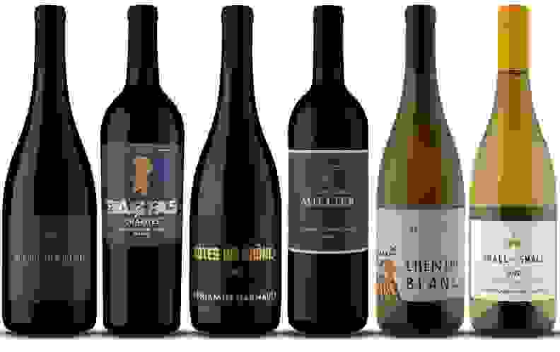 Six bottles of assorted red wines in a row.