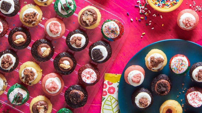A spread of Baked By Melissa's mini cupcakes on a pink background