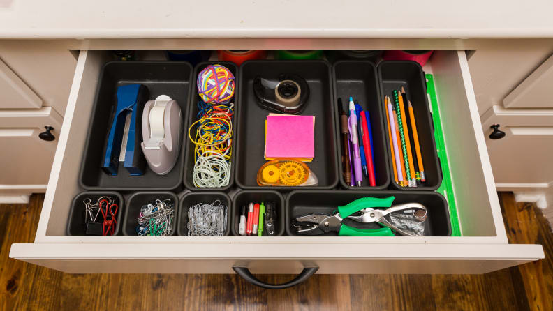 A desk draw open with a variety of organized desk essential items.