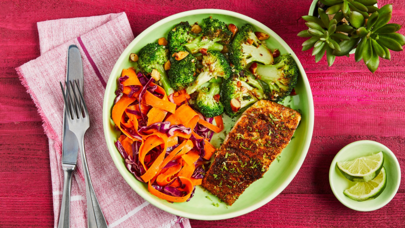 A bright pink table with a food-filled green bowl on it.