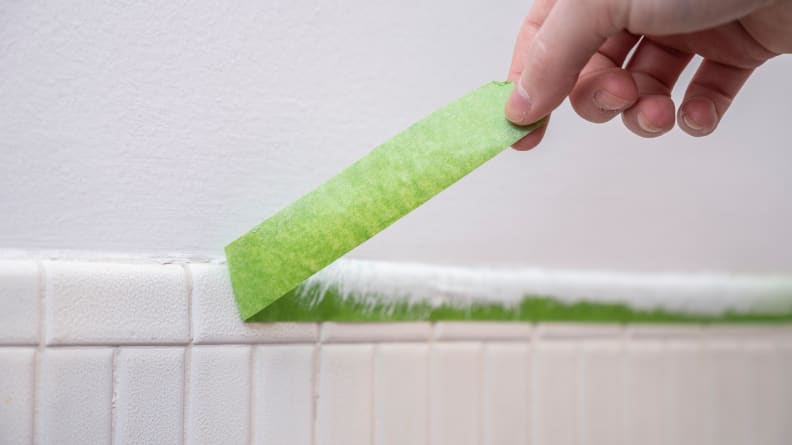 Person pulling off green painter's tape from wall after painting