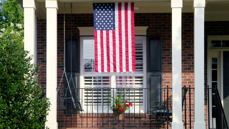 Front porch of brick house with American flag hanging vertically from ceiling outdoors.