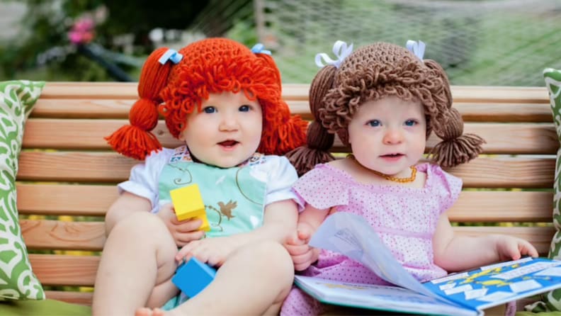 Infants wearing yarn wigs outdoors.