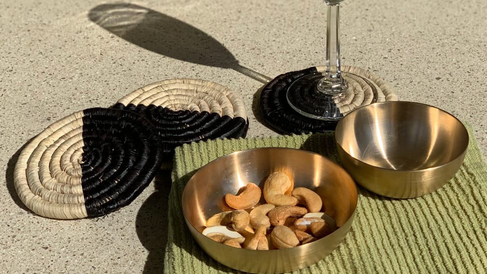 Kansa bronze bowls and handwoven palm leave coasters with a champagne glass and cashews on a green kitchen linen