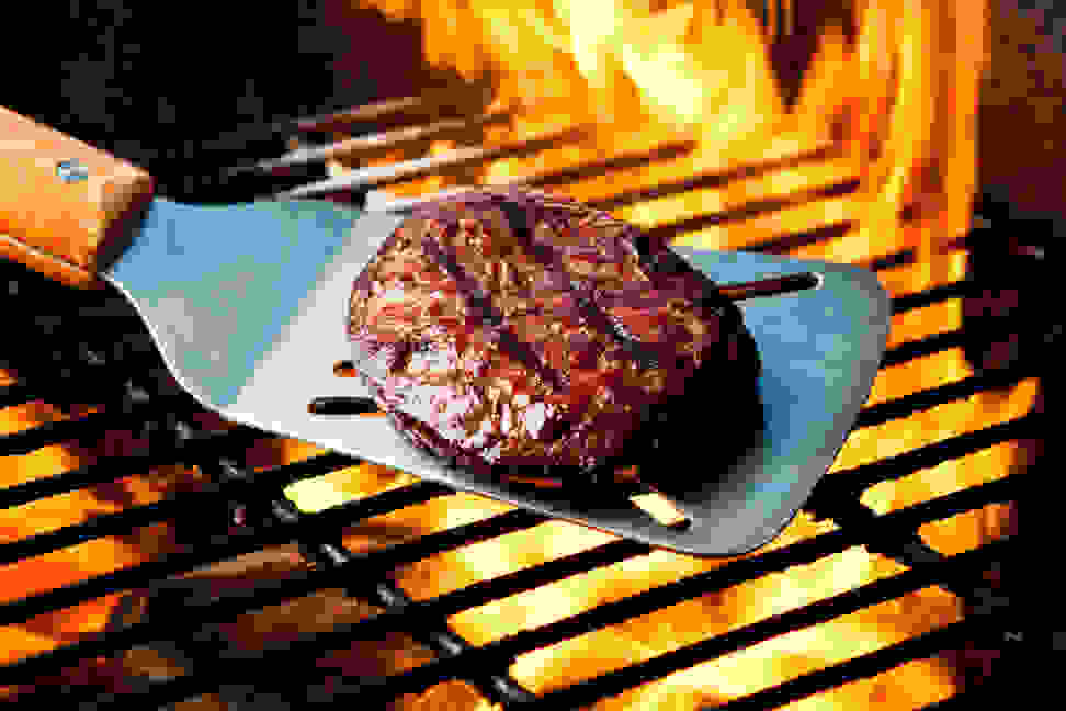 Spatula holding a burger over a flame-covered grill