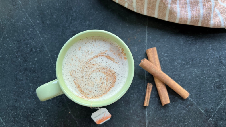 mug of chai tea latte and cinnamon sticks on a dark counter.