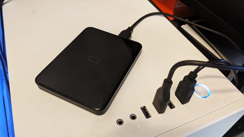 A small external hard drive plugged into the top of a desktop computer case