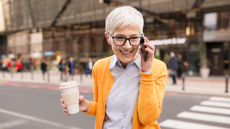 Smiling person talking on cellphone outdoors while holding cup of coffee.