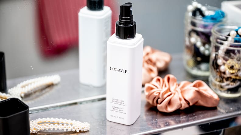 A white square-shaped bottle of hair detangler next to hair accessories