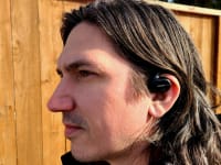 Bose Sport Earbuds listening with earbuds in left ear in front of cedar planks