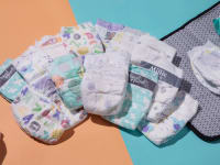 A stack of baby's diapers in the middle a changing mat and baby wipes and a pile of talcum powder.