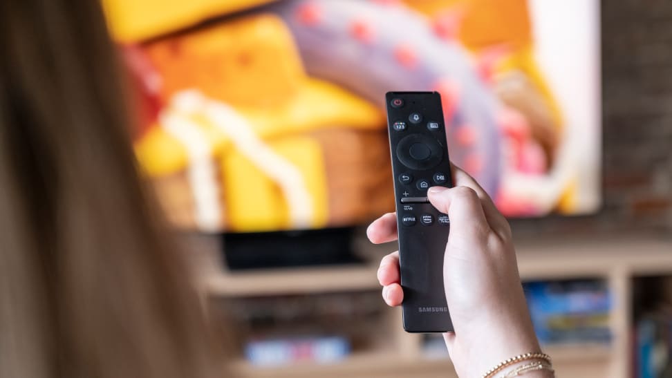 An out-of-focus person holding a Samsung remote control in front of a Samsung TV
