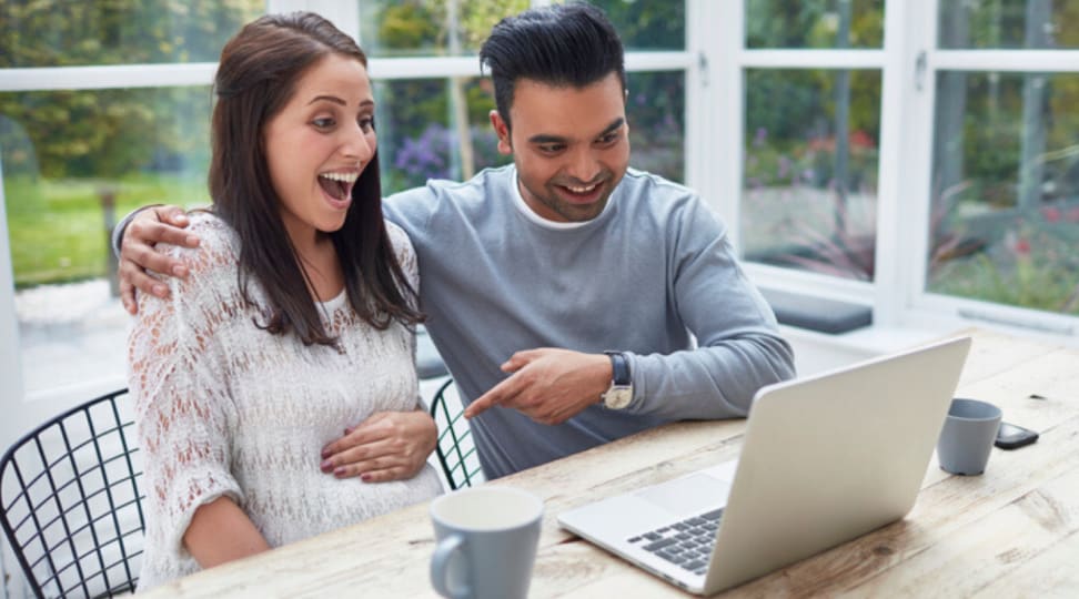 A pregnant woman and man sitting at an outdoor patio table using the computre