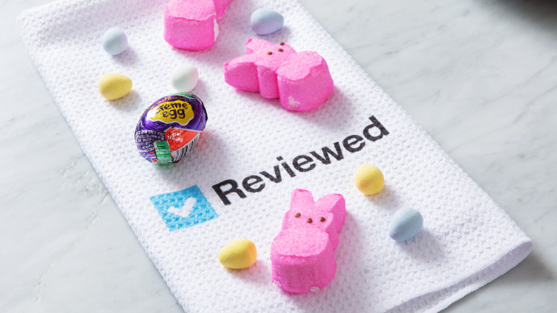 A Reviewed kitchen towel sits on a white counter and is covered with Peeps and Cadbury eggs.