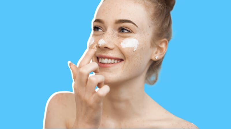 Person smiling while applying facial cream to nose and cheeks.