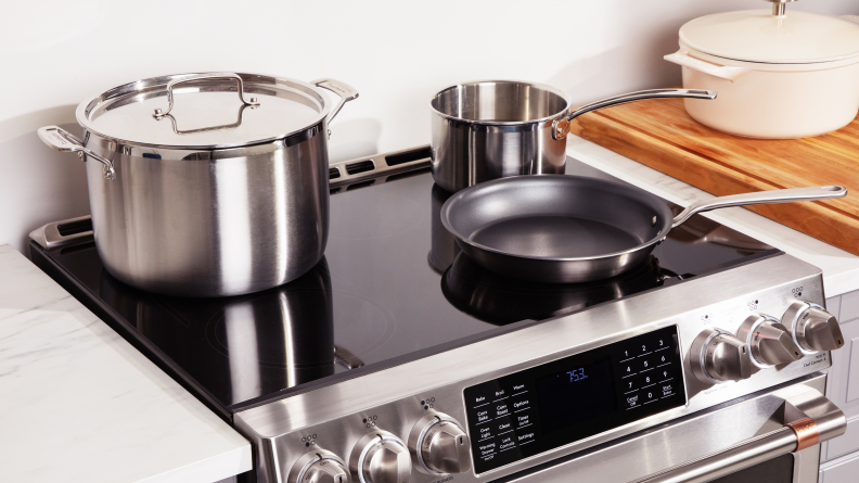 A stainless steel stock pot, sauté pan, and frying pan sit atop the stove of the Café CHS900P2MS1 30-inch Smart Slide-in Induction Range.
