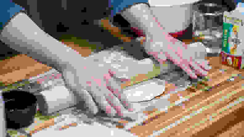 A person using a rolling pin to flatten out a circle of dough.