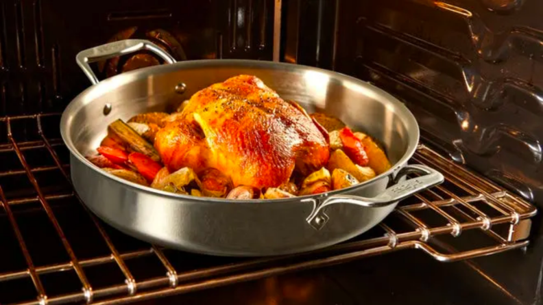 A roasting pan in an oven, with chicken, carrots, and potatoes.