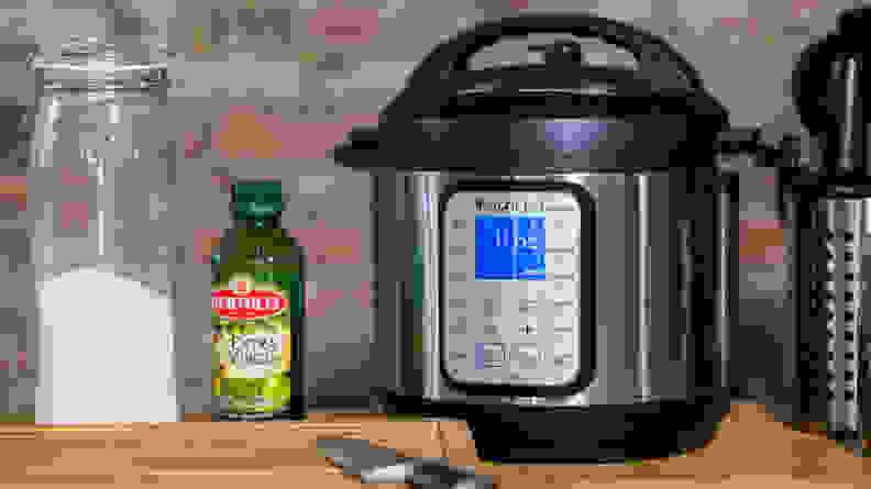 An Instant Pot on a table besides a cutting board a bottle of olive oil and a jar of flour.