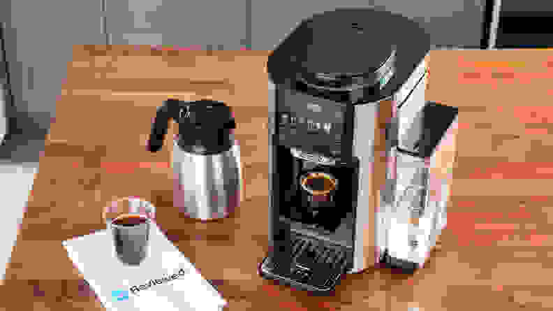 The De'Longhi TrueBrew on a counter next to the carafe and a cup of coffee on a Reviewed napkin.