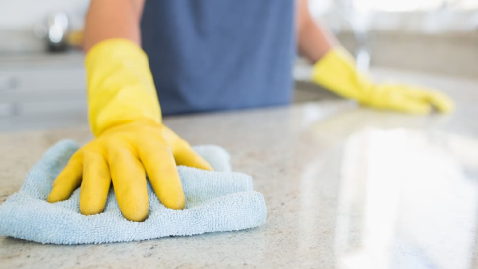Hands with yellow gloves holding blue cleaning towel scrubbing countertop