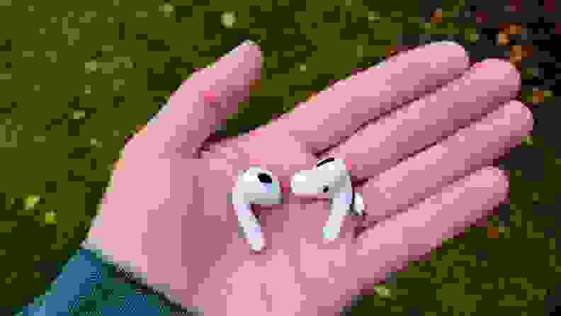 The all-white AirPods (left) next to the all-white AirPods Pro (right) shows similar sizing in the reviewer's hand, but the pro shows a silicone eartip.