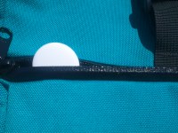 An Apple AirTag resting inside the zipped up pocket of a blue backpack.