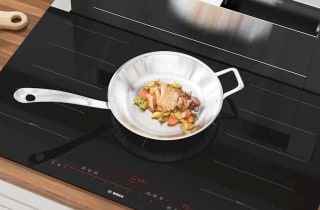 Bosch induction cooktop with chicken cooking on metal pan.