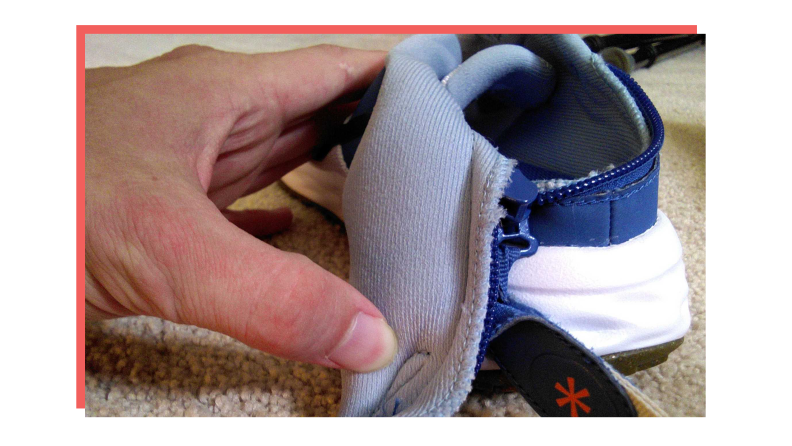 Person using thumb to pull down back strap on white Nike Revolution 6 FlyEase.