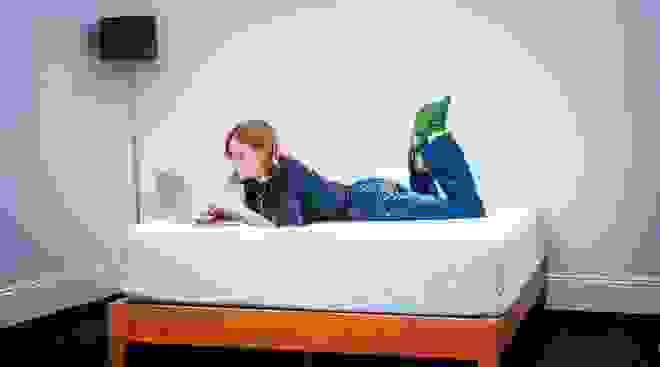 Person laying on mattress while using laptop.