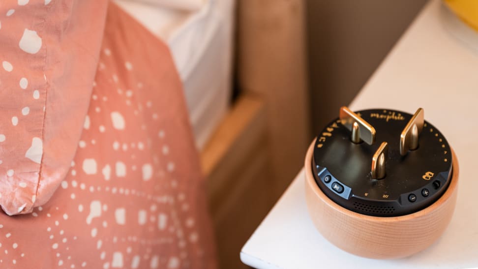 The Morphee, a black and brown speaker with gold keys and decorations, next to a bed with pink covers.