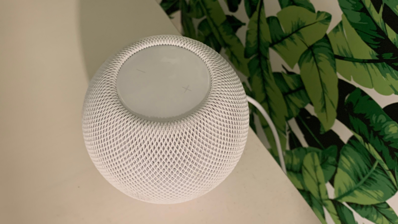 Apple HomePod Mini sits on a white desk.