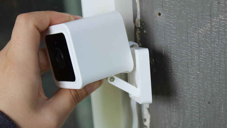 Person mounting Wyze Cam V3 on wall outdoors.