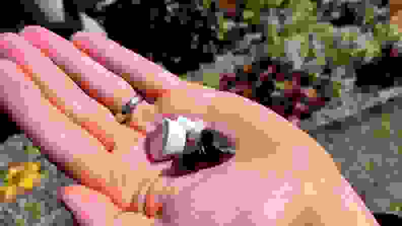 黑色搪瓷Klipsch T5 II真无线ANC耳塞坐在旁边的白色T5 II真无线耳塞在一个开放的手与银结婚戒指。