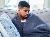 A person lounges on the couch wrapped in a blanket.