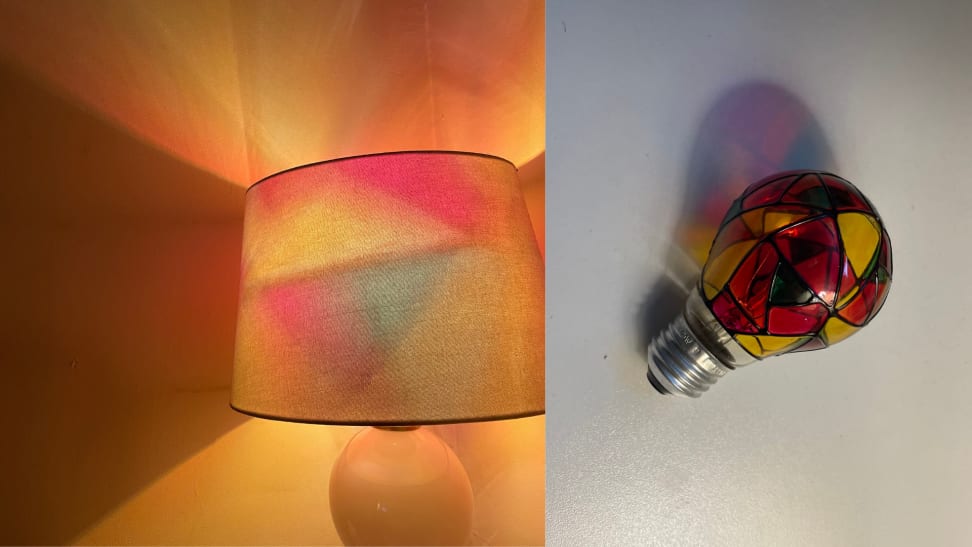 A lamp lights a room with red, yellow and orange light, on right a stained glass light bulb sits on a counter