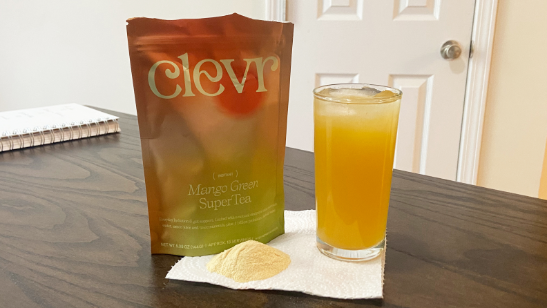 Table with a bag of Clevr Blends Mago Green SuperTea next to a tall glass of the beverage