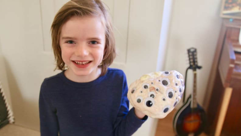 Young boy in blue shirt smiling holding slime with eyeballs mixed in.