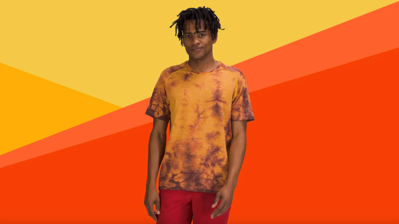 Model wearing orange tie dye shirt and red shorts.