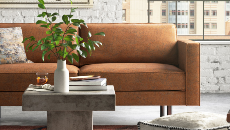 An orange couch with a plant in a vase on a stone table.